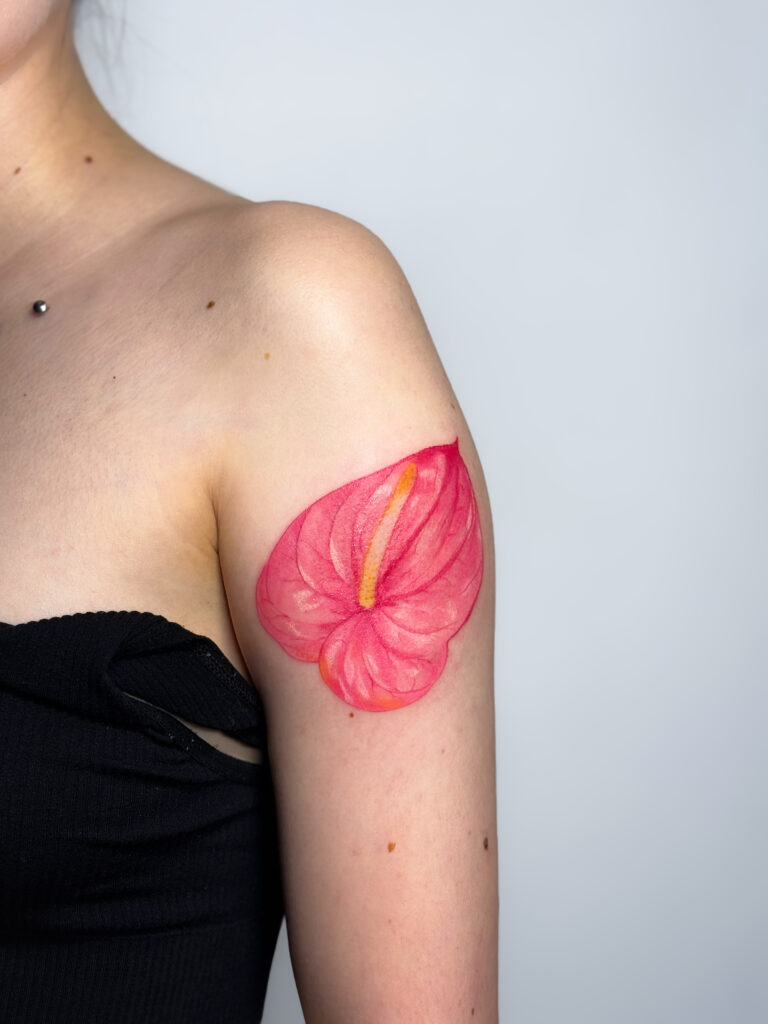 A bright and vivid anthurium bloom tattoo on the shoulder, expressing tropical elegance.