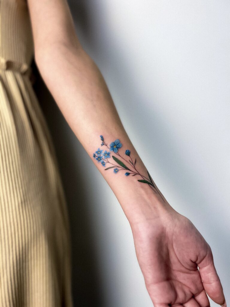 Delicate blue floral tattoo on the wrist, symbolizing grace and simplicity with a natural look.