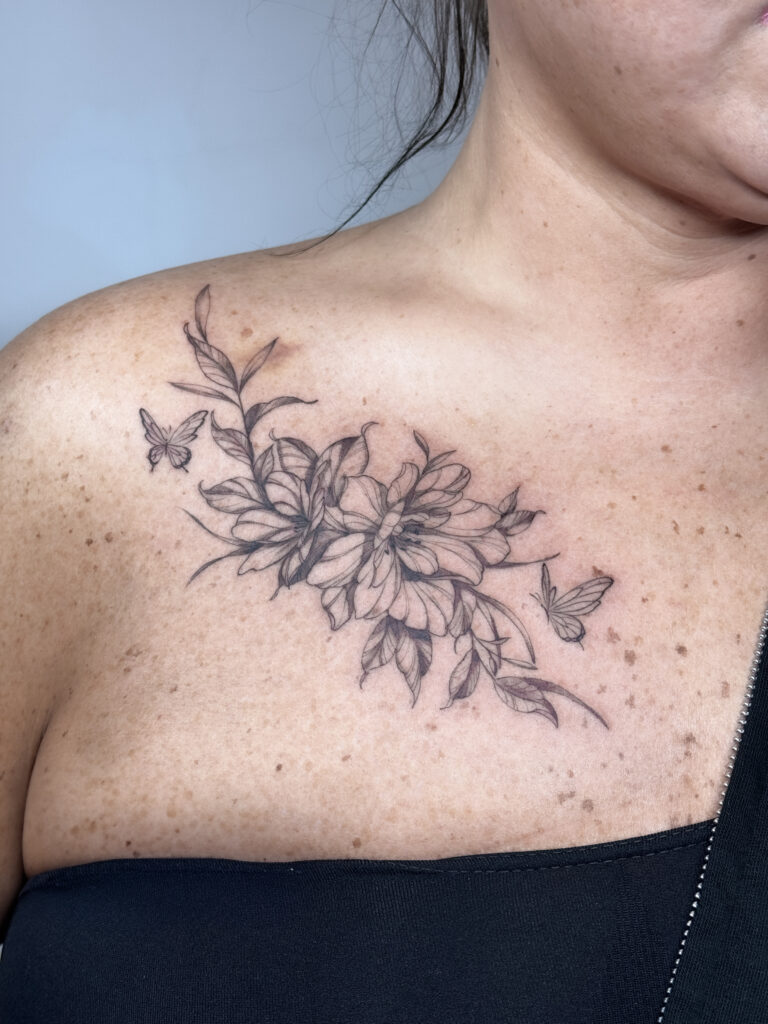 Fineline tattoo of blooming flowers and butterflies on the chest, executed in delicate lines.