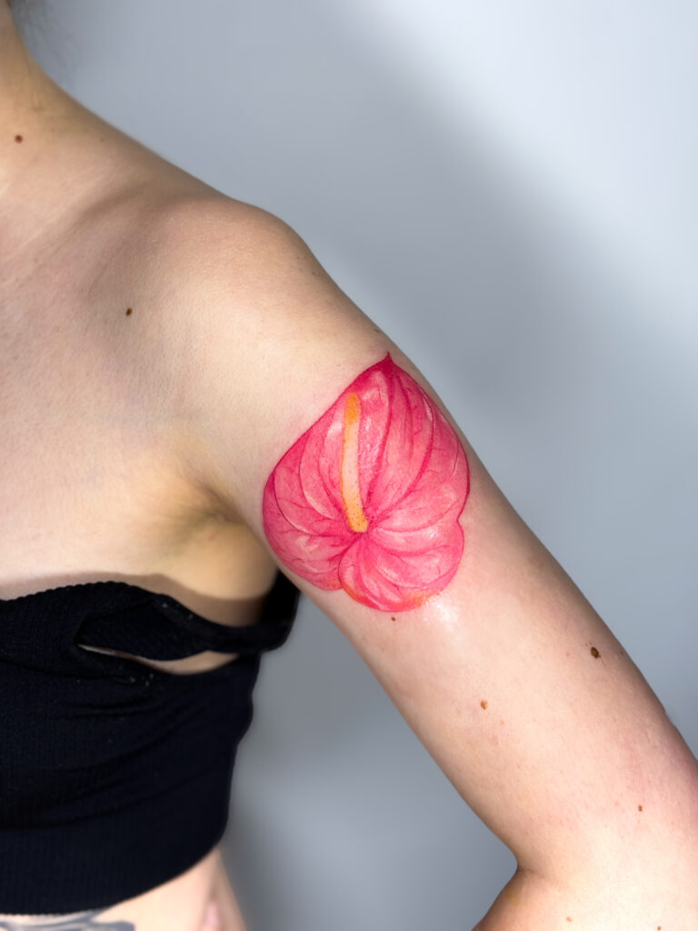 Colorful anthurium flower tattoo on the arm, featuring vibrant pink and yellow tones.