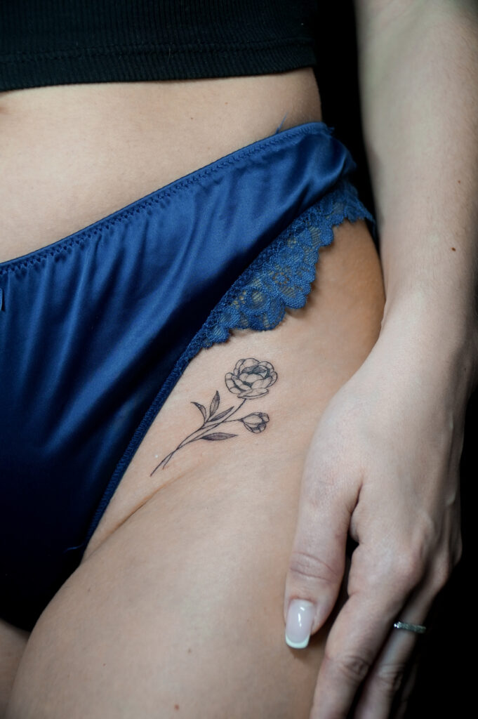 Minimalistyczny tatuaż z kwiatem na udzie w stylu fineline, delikatny i elegancki wzór wykonany w Fineline Tattoo Gallery Kraków.