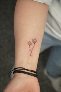 A minimalist fine line tattoo on the wrist, featuring two delicately drawn flowers with intertwined stems. A subtle and elegant design perfect for those who appreciate simplicity and symbolic art.