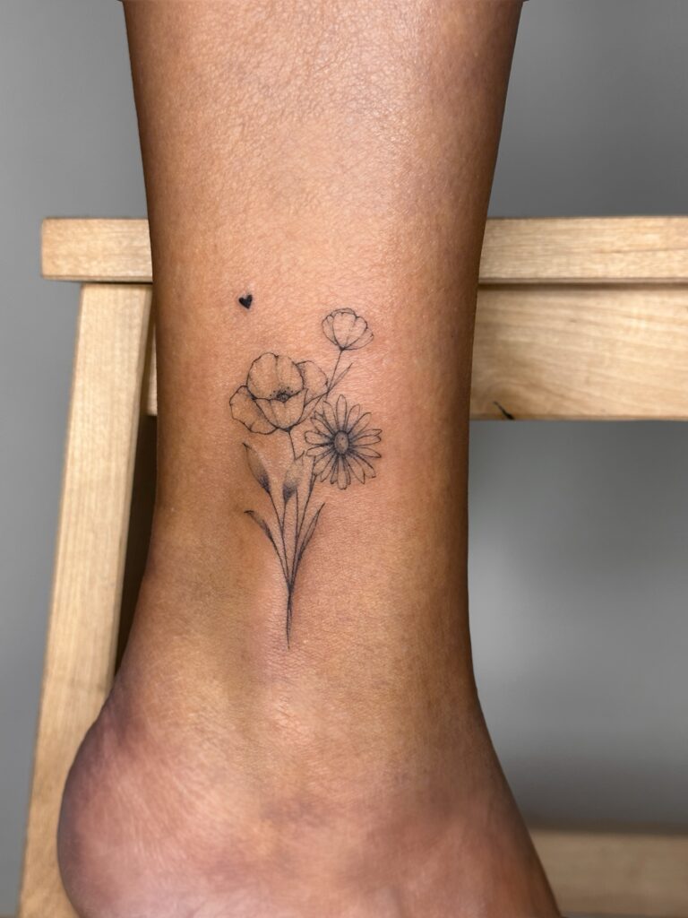 Botanical fine line wildflower tattoo in black ink placed on the ankle. A delicate and feminine composition featuring subtle floral elements, created at Fineline Tattoo Gallery in Krakow.
