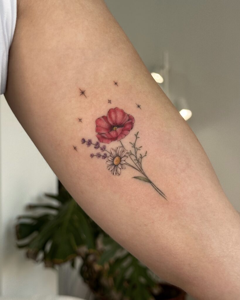 Botanical fine line wildflower tattoo with soft color details, featuring poppy, daisy and lavender, placed on the arm. A delicate and feminine floral composition created at Fineline Tattoo Gallery in Krakow.
