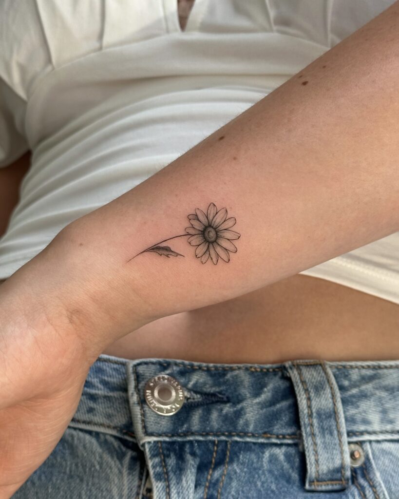 Delicate botanical fine line daisy tattoo in black ink placed on the wrist. A minimal and feminine floral design created at Fineline Tattoo Gallery in Krakow.