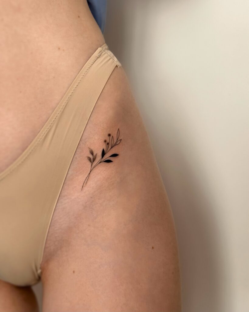 Botanical fine line leaf tattoo in black ink placed on the hip. A minimal and feminine nature-inspired design created at Fineline Tattoo Gallery in Krakow.