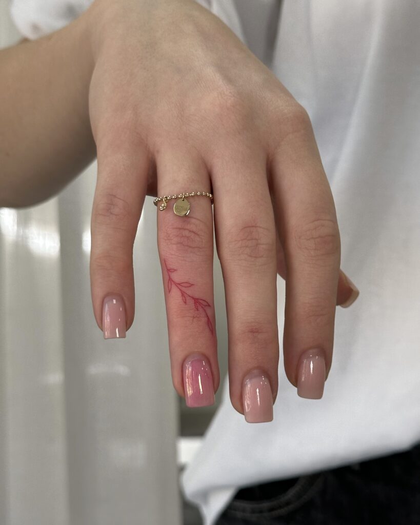 Botanical fine line leaf tattoo in red ink placed on the finger. A delicate and minimal feminine design created at Fineline Tattoo Gallery in Krakow.