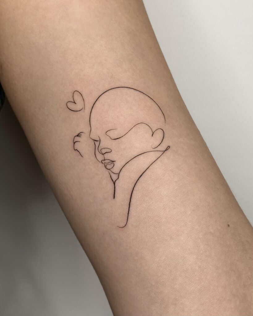 Minimal fine line baby portrait tattoo in black ink placed on the arm. A delicate and emotional line art design symbolizing love and connection, created at Fineline Tattoo Gallery in Krakow.