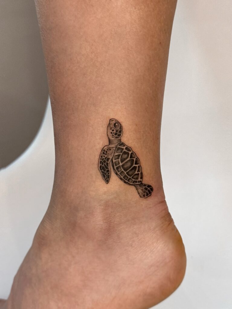 Fine line sea turtle tattoo in black ink placed on the ankle. A minimal and symbolic ocean-inspired design created at Fineline Tattoo Gallery in Krakow.