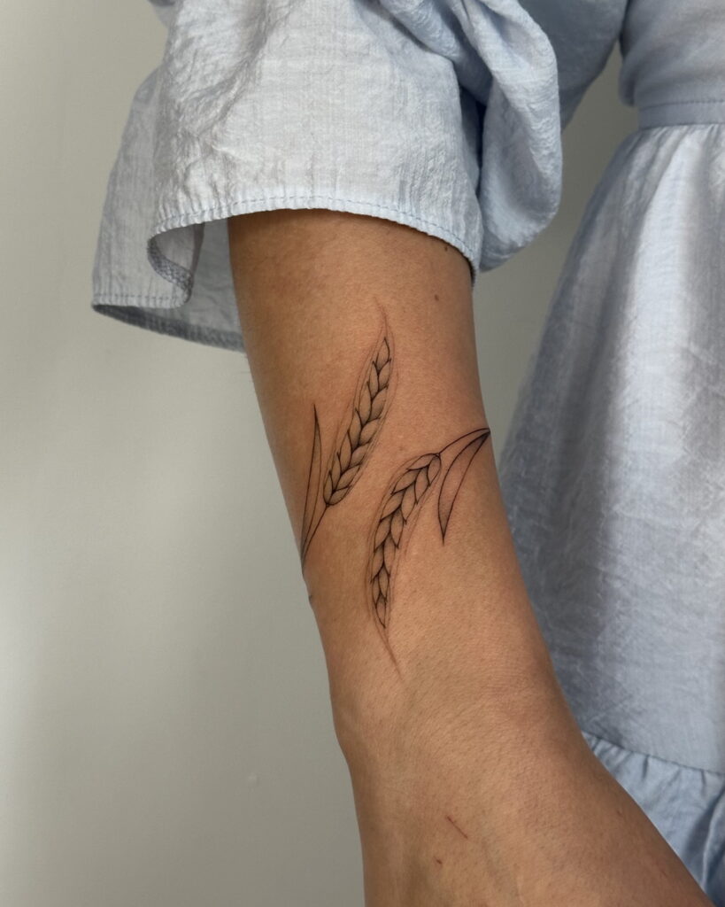 Minimal fine line wheat tattoo in black ink placed on the arm. A delicate and nature-inspired design created at Fineline Tattoo Gallery in Krakow.