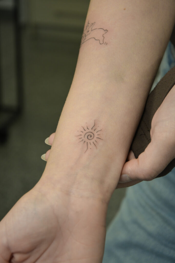 Delikatny tatuaż słońca wykonany podczas szkolenia Mini Tattoo — minimalistyczny wzór ćwiczony przez początkującą kursantkę w trakcie praktycznej części warsztatów.