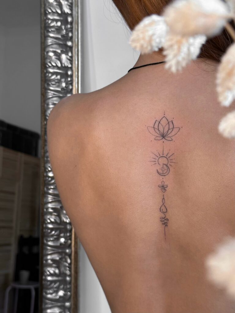 Ornamental fine line spine tattoo featuring a lotus and crescent moon in black ink. A delicate and symbolic vertical design created at Fineline Tattoo Gallery in Krakow.