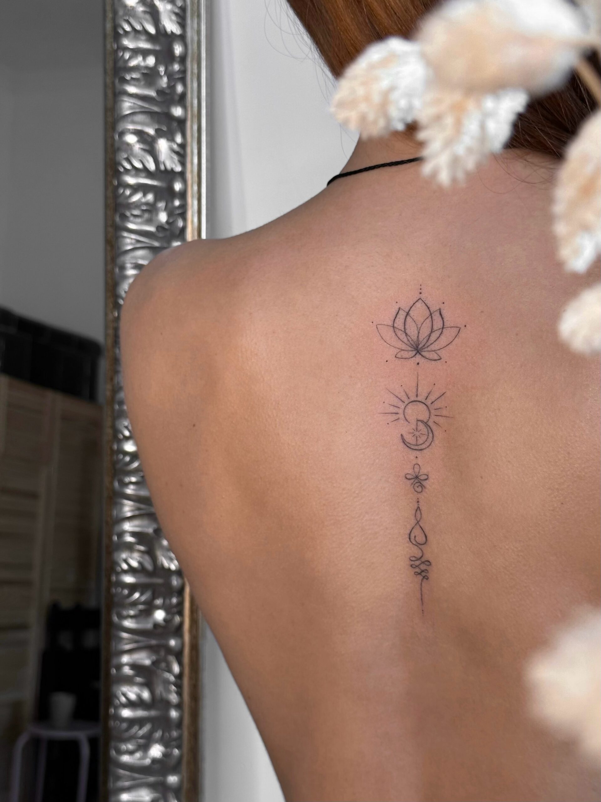 Ornamental fine line spine tattoo featuring a lotus and crescent moon in black ink. A delicate and symbolic vertical design created at Fineline Tattoo Gallery in Krakow.