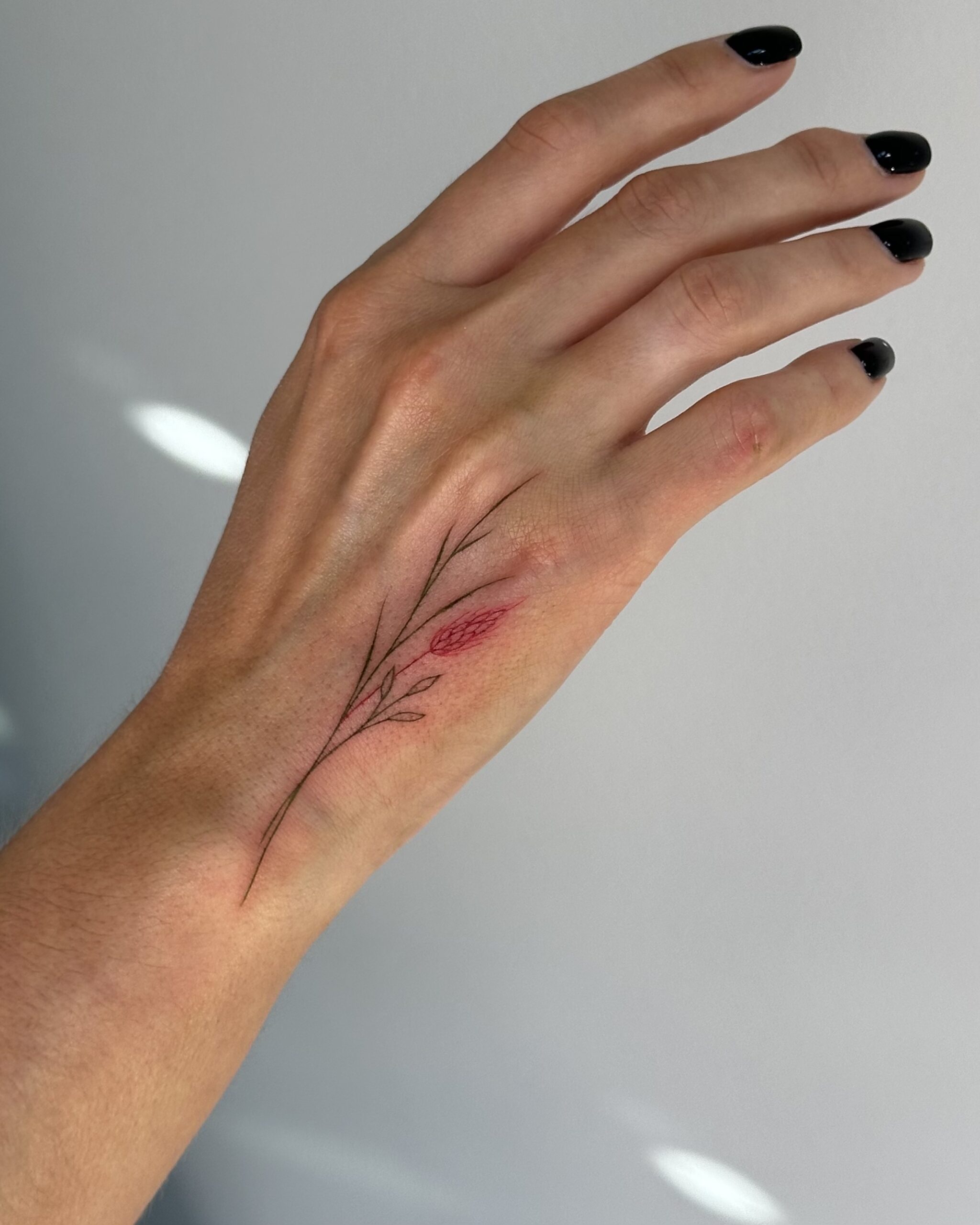 Delicate fine line floral tattoo with a soft red blossom, placed on the hand. A subtle and elegant botanical design created at Fineline Tattoo Gallery in Krakow.