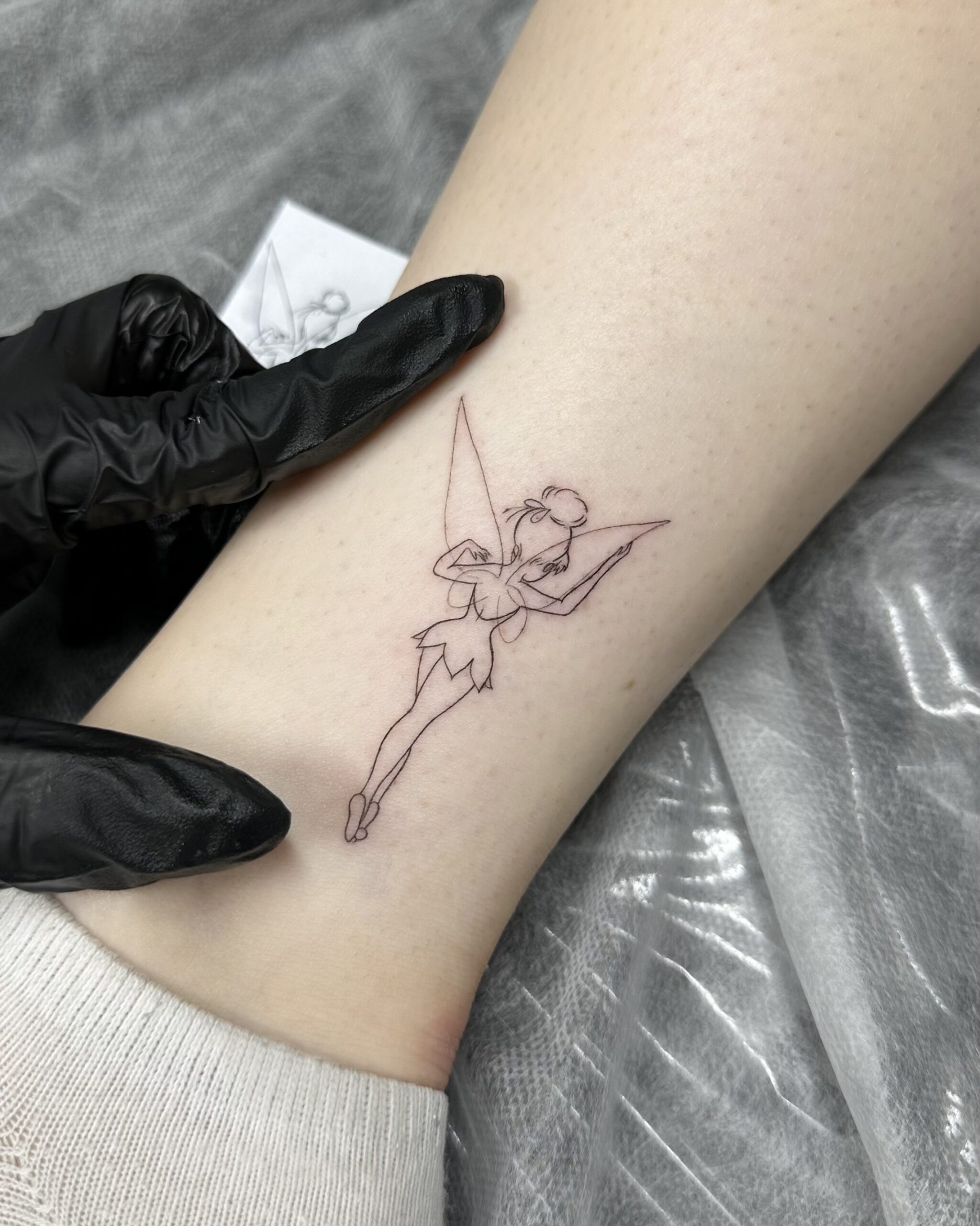 Minimalist fine line tattoo of Tinker Bell placed on the ankle. A subtle, airy and charming fairy design created at Fineline Tattoo Gallery in Krakow.