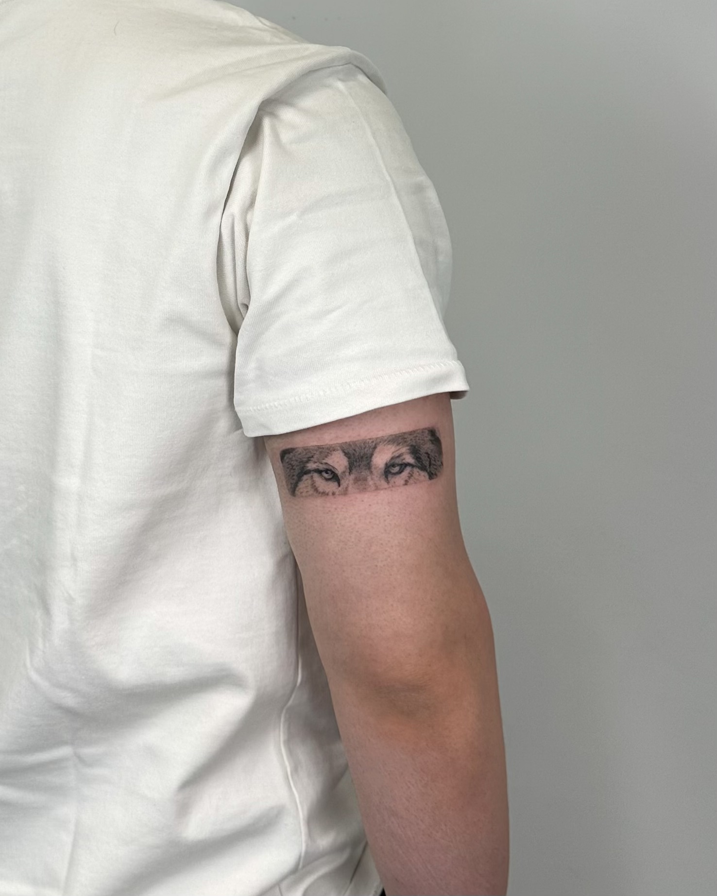 Realistic wolf eyes tattooed as a subtle arm band. Detailed shading and strong gaze create a powerful and symbolic design, made at Fineline Tattoo Gallery in Krakow.