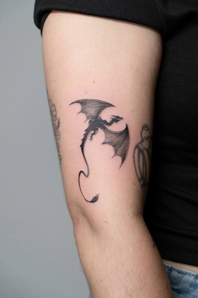 A subtle fine line dragon tattoo with outstretched wings, placed on the arm. Perfect for fantasy lovers and those seeking a symbol of strength and independence.