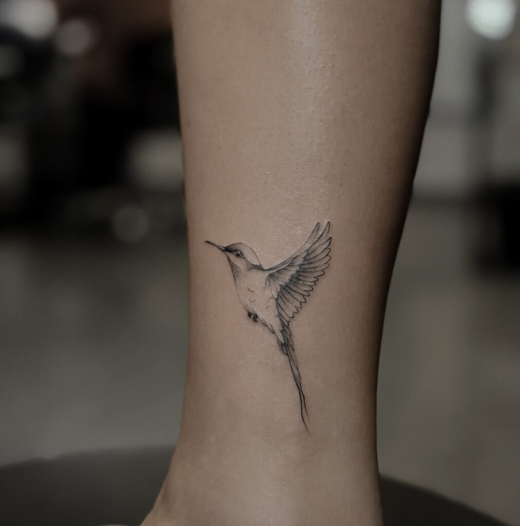 Pierwsza praca kursantki wykonana podczas szkolenia tatuażu. Delikatny tatuaż fineline przedstawiający kolibra, zrealizowany w ramach nauki technik tatuowania.