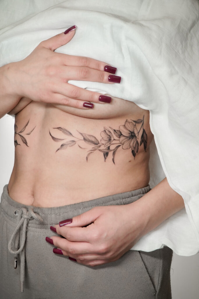 Delikatny czarno-szary tatuaż kwiatowy wykonany w stylu fine line, umieszczony na boku tułowia. Elegancka, subtelna kompozycja idealna dla osób szukających kobiecego, roślinnego motywu.