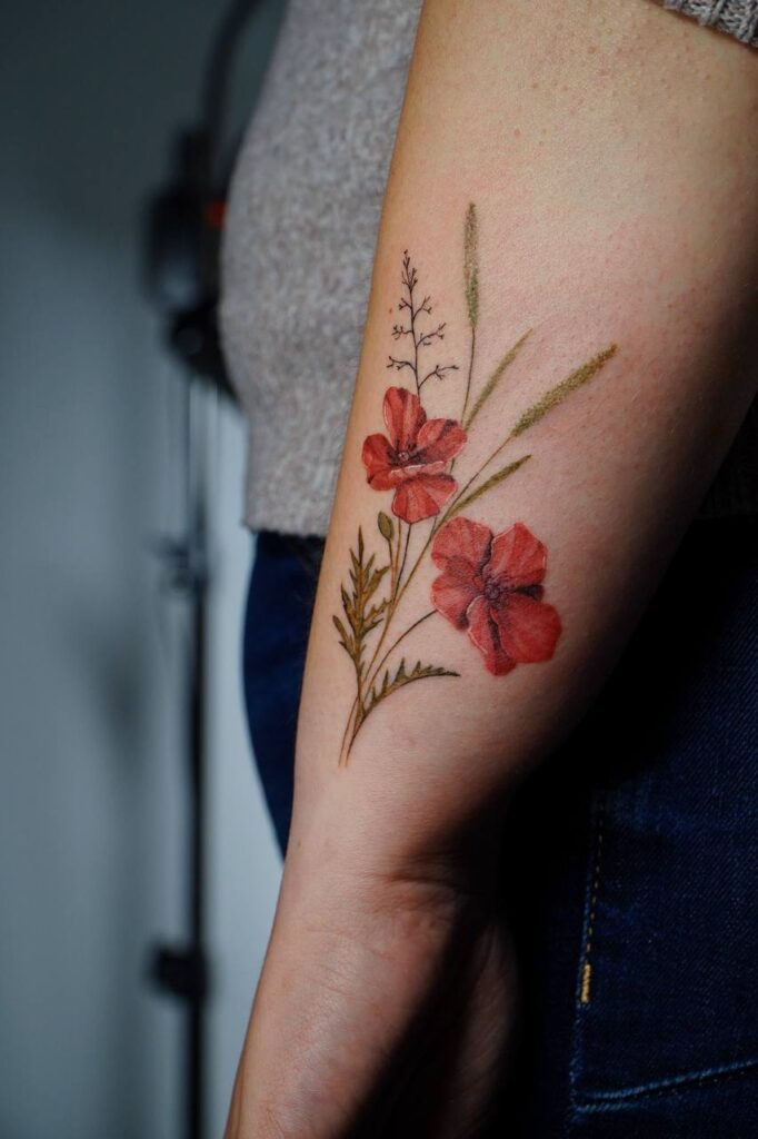 Kolorowy tatuaż maków na przedramieniu w stylu fine line. Subtelna, naturalna kompozycja z czerwonymi kwiatami i delikatnymi gałązkami — idealny wybór dla osób szukających eleganckiego, botanicznego wzoru.
